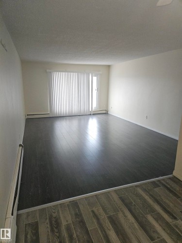 Spacious room featuring dark wood-finish flooring, light-colored walls, and a sliding glass door with vertical blinds - 401 10615 110 Street, Edmonton, AB 