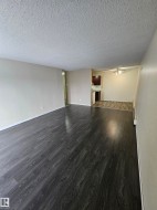 Spacious living area featuring dark wood-finish flooring, light neutral-toned walls, and a textured ceiling - 