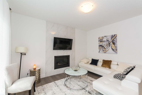 Contemporary living area featuring a tiled fireplace with an integrated television mount, a flush-mount ceiling light, and wood-finish flooring - 15168 16 Street Nw, Edmonton, AB 