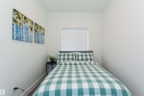 Bedroom featuring light-tone wood-finish flooring, a window with horizontal blinds, and white painted walls - 15168 16 Street Nw, Edmonton, AB 