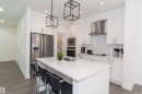 Contemporary kitchen featuring a large central island with an undermount double sink, white cabinetry with silver hardware, stainless steel appliances, a white subway tile backsplash, and recessed and pendant lighting - 15168 16 Street Nw, Edmonton, AB 