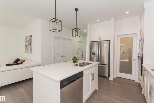Kitchen featuring a central island with dual sinks, white shaker cabinetry, stainless steel appliances, and two pendant lights - 15168 16 Street Nw, Edmonton, AB 