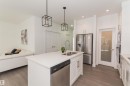 Kitchen featuring a central island with dual sinks, white shaker cabinetry, stainless steel appliances, and two pendant lights - 15168 16 Street Nw, Edmonton, AB 