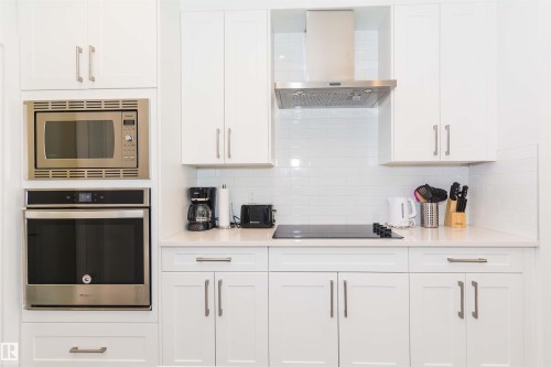 Modern kitchen featuring white shaker cabinetry, stainless steel built-in microwave and oven, a sleek cooktop, and a matching stainless steel range hood - 15168 16 Street Nw, Edmonton, AB 