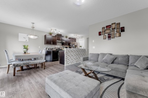 Open-concept living space featuring wood-finish flooring, a kitchen with dark cabinetry, a breakfast bar with mosaic tile detailing, recessed lighting, and a dining area illuminated by a modern pendant light - 1532 33B Street, Edmonton, AB 