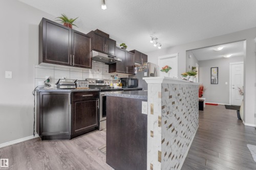 Kitchen featuring dark wood-finish cabinetry, stainless steel appliances, and a tiled backsplash - 1532 33B Street, Edmonton, AB 