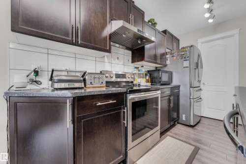 Kitchen featuring dark wood-finish cabinetry, stainless steel appliances, a white tile backsplash, and wood-finish flooring - 1532 33B Street, Edmonton, AB 