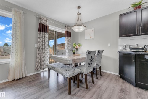 Bright dining area featuring wood-finish flooring, a contemporary chandelier, and a sliding glass door to the exterior - 1532 33B Street, Edmonton, AB 