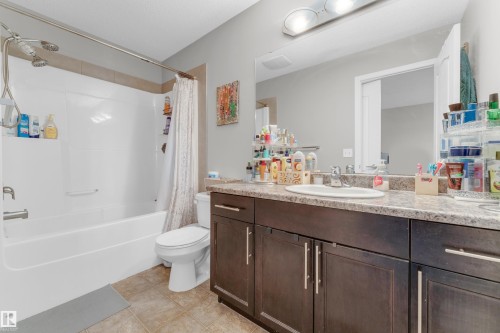 Bathroom featuring a tub/shower combination with a dual shower head fixture, a single vanity with a white basin sink, dark wood-finish cabinetry, and a light-toned countertop - 1532 33B Street, Edmonton, AB 