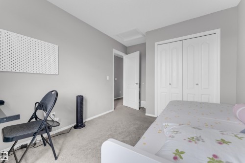 Bedroom featuring light gray wall paint, gray carpet flooring, white bi-fold closet doors, a white baseboard, and a white interior door - 1532 33B Street, Edmonton, AB 