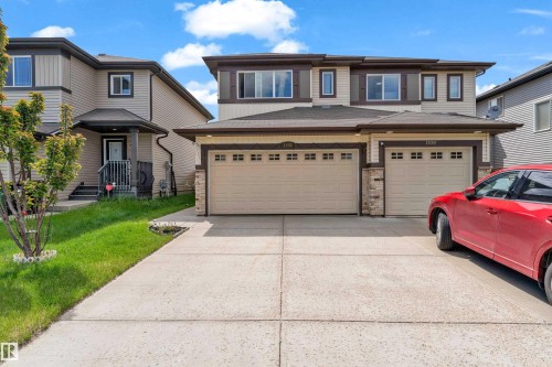 Modern duplex exterior featuring dual attached garages, a concrete driveway, two-tone siding, stone accents, and a covered front entry - 1532 33B Street, Edmonton, AB 