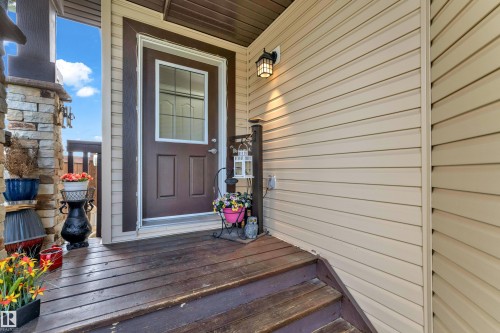 Front entry featuring a dark brown door with decorative glass, beige horizontal siding, a stone-clad pillar, and a matching dark brown wooden deck and stairs - 1532 33B Street, Edmonton, AB 