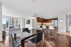 Open-concept living space featuring wood-finish flooring throughout, a modern kitchen with rich wood cabinetry and stainless steel appliances, and a peninsula with counter seating - 