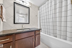 Bathroom featuring a dark wood-finish vanity with a dark countertop, an undermount sink with a brushed nickel faucet, a framed mirror, and a white tiled shower/tub combination - 