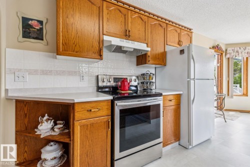 Kitchen featuring wood cabinetry, white tile backsplash, light-toned countertops, and light flooring - 5131 152A Avenue, Edmonton, AB 