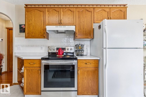 Kitchen featuring wood cabinetry, white countertops, white tile backsplash, stainless steel range, and a white refrigerator - 5131 152A Avenue, Edmonton, AB 