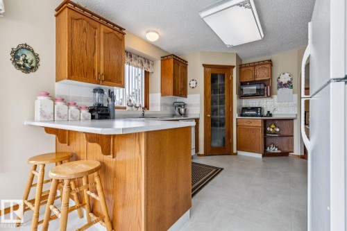 Kitchen featuring wood-finish cabinetry, white countertops, and white tile backsplash - 5131 152A Avenue, Edmonton, AB 
