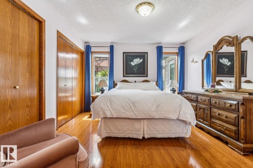 Spacious bedroom featuring wood-finish flooring, two sets of bi-fold closet doors, and two windows - 5131 152A Avenue, Edmonton, AB 