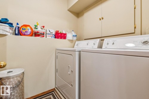 Dedicated laundry area featuring built-in cabinetry, a utility shelf, light-toned walls, and a patterned floor mat - 5131 152A Avenue, Edmonton, AB 