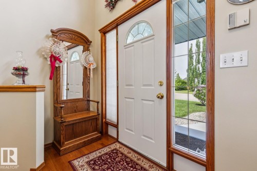 Entryway featuring wood-finish flooring, a white paneled entry door with an arched transom, and a sidelight with grid details - 5131 152A Avenue, Edmonton, AB 