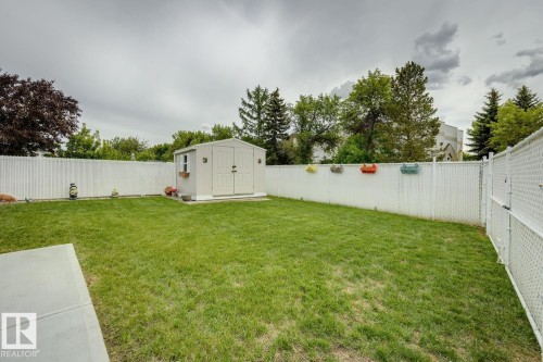 Spacious backyard featuring a manicured lawn, a concrete patio, and a white chain-link fence providing enclosure - 5131 152A Avenue, Edmonton, AB 