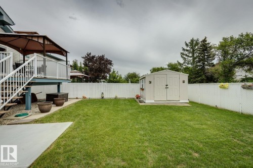 Expansive grassy yard featuring a white privacy fence, a detached storage shed, a multi-level deck with a brown canopy, and a concrete patio - 5131 152A Avenue, Edmonton, AB 