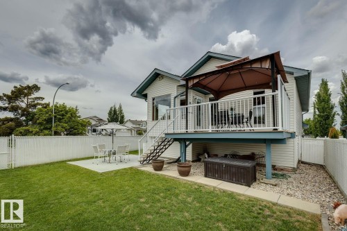Rear exterior featuring a raised deck with white railings, a lower concrete patio, and a manicured lawn - 5131 152A Avenue, Edmonton, AB 