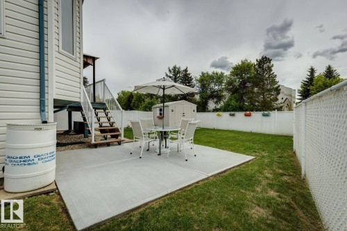 Expansive backyard featuring a concrete patio, green lawn, white privacy fence, and an exterior storage shed - 5131 152A Avenue, Edmonton, AB 