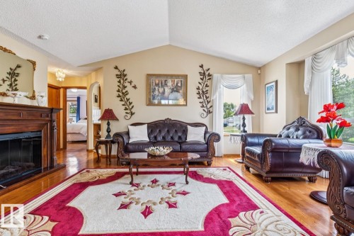 Spacious living area featuring vaulted ceilings, wood-finish flooring, a built-in fireplace with a carved wood mantel, and expansive windows - 5131 152A Avenue, Edmonton, AB 