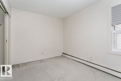Carpeted room featuring a white window frame, horizontal window blinds, baseboard heating, and a textured ceiling - 71 11255 31 Avenue, Edmonton, AB - Indoor Photo Showing Other Room
