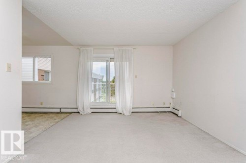 Spacious room featuring light-toned carpeting and a sliding glass door with white sheer curtains - 71 11255 31 Avenue, Edmonton, AB - Indoor Photo Showing Other Room