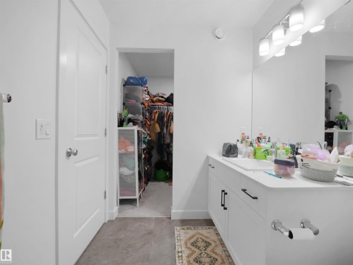 Bathroom vanity featuring a single integrated sink, white cabinetry with black hardware, and a large wall-mounted mirror - 19316 29 Avenue, Edmonton, AB 