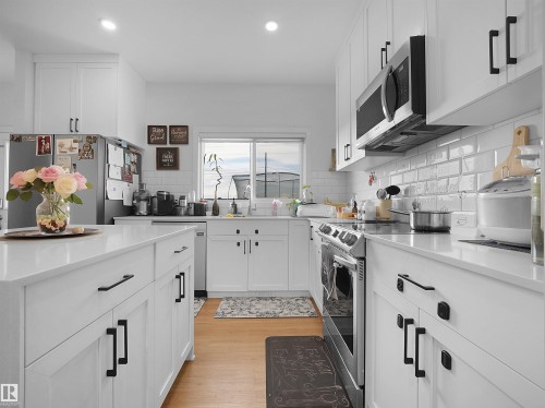 Bright kitchen featuring white cabinetry with black hardware, stainless steel appliances, a white subway tile backsplash, and light wood-finish flooring - 19316 29 Avenue, Edmonton, AB 