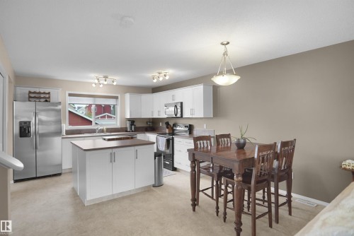Kitchen with stainless steel appliances, white cabinetry, a central island with a wood-finish countertop, and a dining area featuring a dark wood table with matching chairs - 292 Simmonds Way, Leduc, AB 