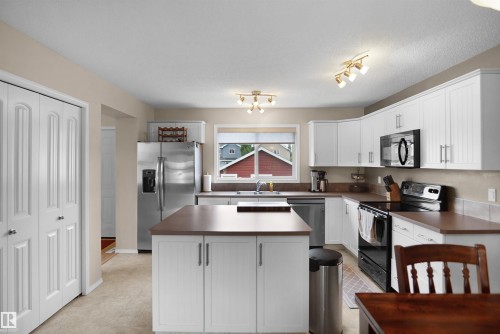 Kitchen featuring white cabinetry, a central island with a brown countertop, stainless steel appliances, and track lighting fixtures - 292 Simmonds Way, Leduc, AB 