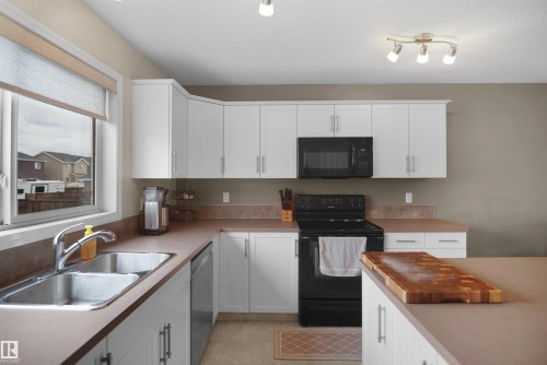 Kitchen featuring white cabinetry, a double basin stainless steel sink, black built-in microwave, black electric range, and light brown countertops - 292 Simmonds Way, Leduc, AB 