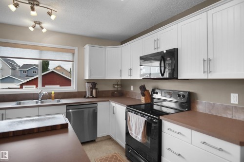 Kitchen featuring white cabinetry, a double basin sink, black appliances, track lighting, and a window - 292 Simmonds Way, Leduc, AB 