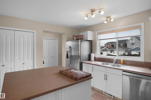 Kitchen featuring white cabinetry, stainless steel appliances, a double basin sink, and a central island with a wood-finish countertop - 292 Simmonds Way, Leduc, AB 