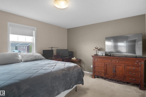 Carpeted bedroom featuring a large window with white trim, a flush-mount ceiling light fixture, and neutral-toned wall paint - 292 Simmonds Way, Leduc, AB 