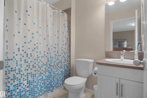 Bathroom featuring a white vanity with double-door cabinetry, an integrated sink, a neutral countertop, and a wall-mounted mirror with overhead lighting - 292 Simmonds Way, Leduc, AB 