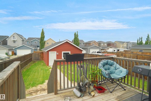 Expansive wooden deck with a slatted railing, providing access to a grassy yard with a detached red garage - 292 Simmonds Way, Leduc, AB 