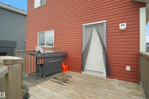 Exterior deck with wood planks, featuring a white door, a sliding window, and red siding - 292 Simmonds Way, Leduc, AB 