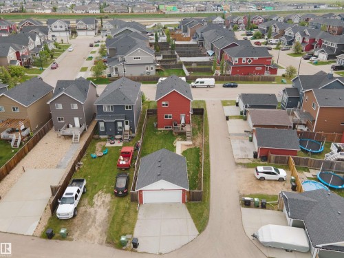 Red two-story home featuring a detached garage with a white door, a spacious backyard with green lawn, and a light-colored fence enclosing the property - 292 Simmonds Way, Leduc, AB 