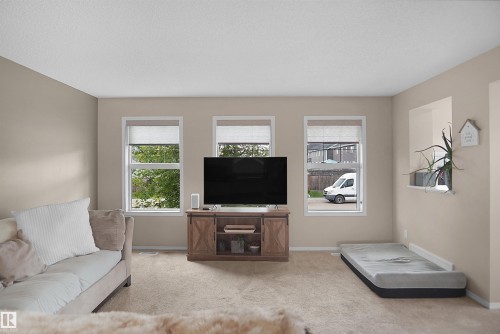 Light-filled living area featuring three distinct windows, neutral wall tones, and a built-in decorative niche - 292 Simmonds Way, Leduc, AB 