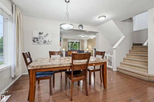 Spacious dining area featuring wood-finish flooring, a contemporary chandelier, large windows with natural light, and an open concept overlooking the living area - 1804 121 Street, Edmonton, AB 