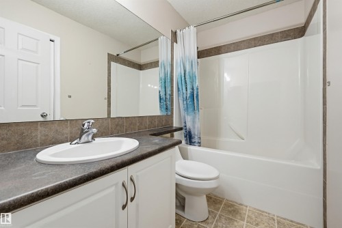 Bathroom featuring a vanity with a drop-in sink, a built-in bathtub with a shower, and neutral tile flooring - 1804 121 Street, Edmonton, AB 
