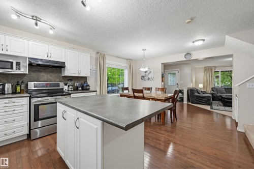 Kitchen featuring a central island with a solid surface countertop, white cabinetry with dark hardware, stainless steel appliances, and wood-finish flooring - 1804 121 Street, Edmonton, AB 