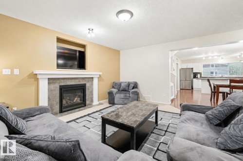 Living area featuring a gas fireplace with a tiled surround and white mantel, a television niche, recessed lighting, and a broad arched opening into a kitchen with wood-finish flooring - 1804 121 Street, Edmonton, AB 