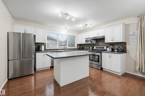 Kitchen featuring dark wood-finish flooring, white cabinetry, stainless steel appliances, and a central island with a dark countertop - 1804 121 Street, Edmonton, AB 