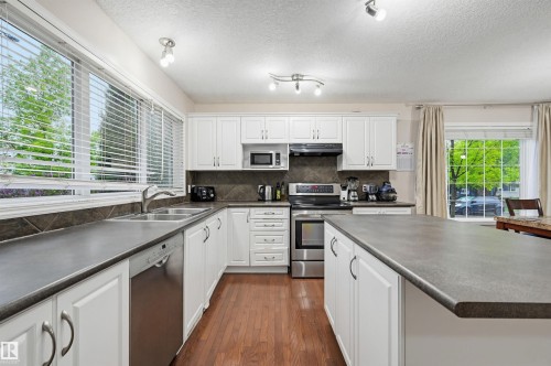 Kitchen featuring white cabinetry, dark countertops, and wood-finish flooring - 1804 121 Street, Edmonton, AB 